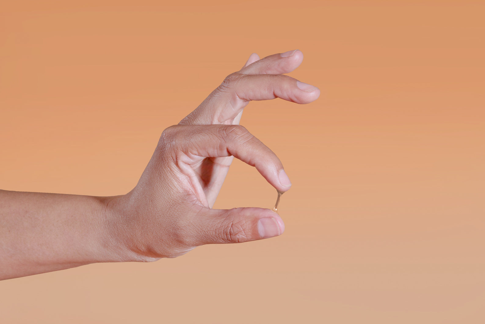 Hand showing Sutil Luxe viscosity against a gradient orange background
