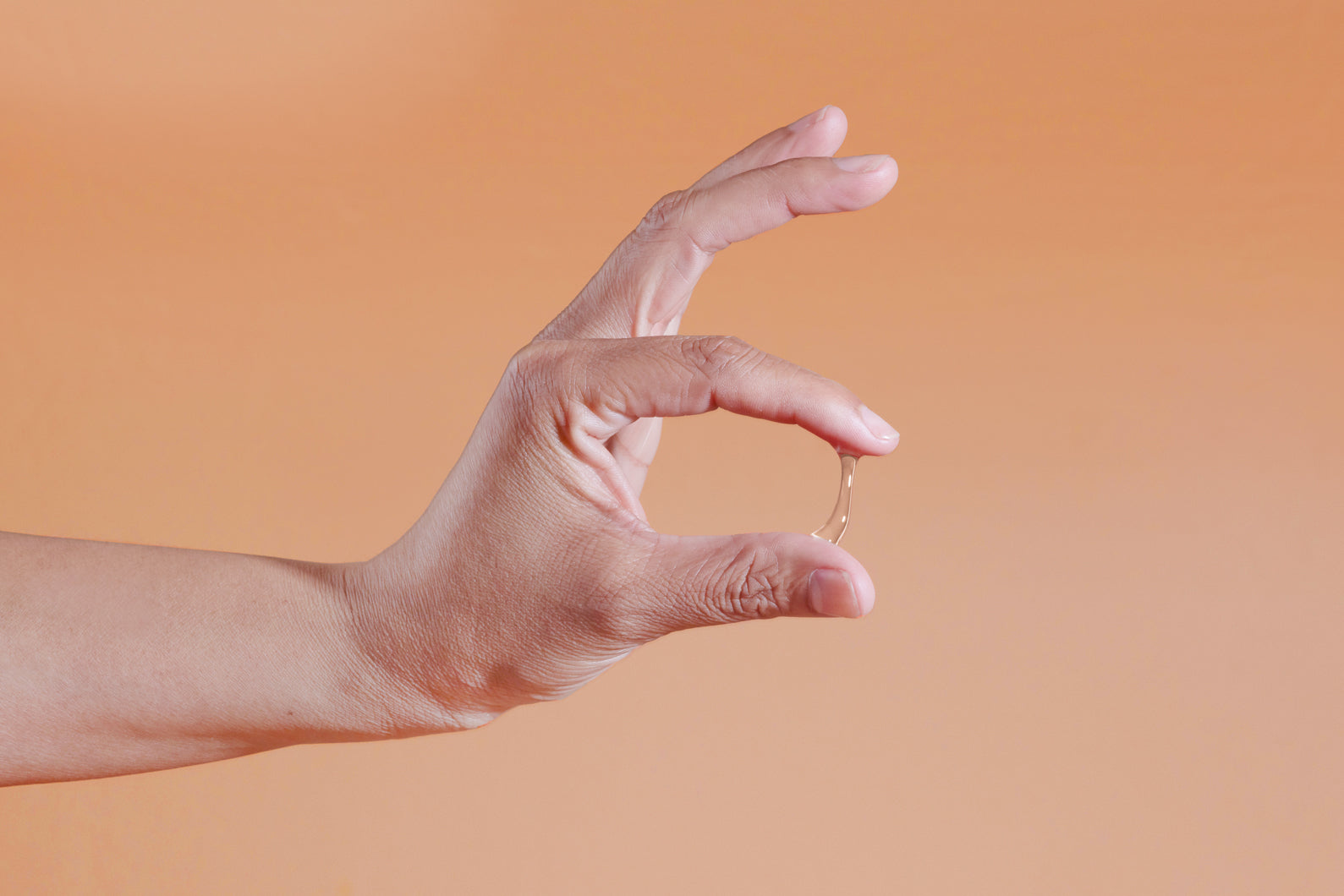 Hand showing Sutil Rich viscosity against a gradient orange background